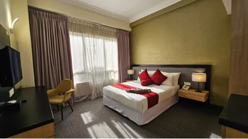Spacious hotel room with a king-sized bed, red accents, and large window at EPF Learning Campus