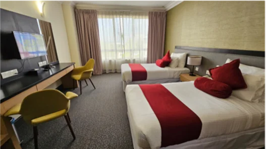 Twin hotel room with two beds, red accents, TV and yellow chairs at EPF Learning Campus