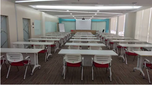 Training room with rows of white tables, red chairs and a projector screen