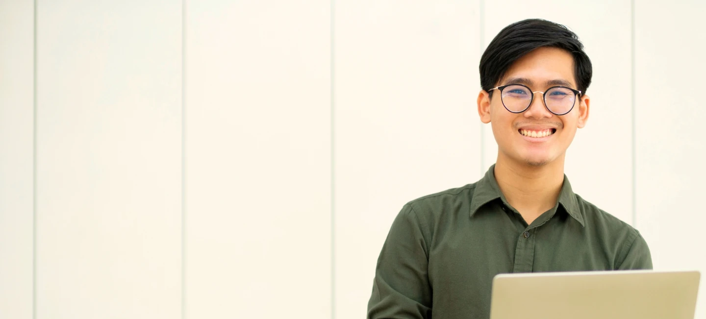Person with glasses uses laptop, smiling in a focused setting.