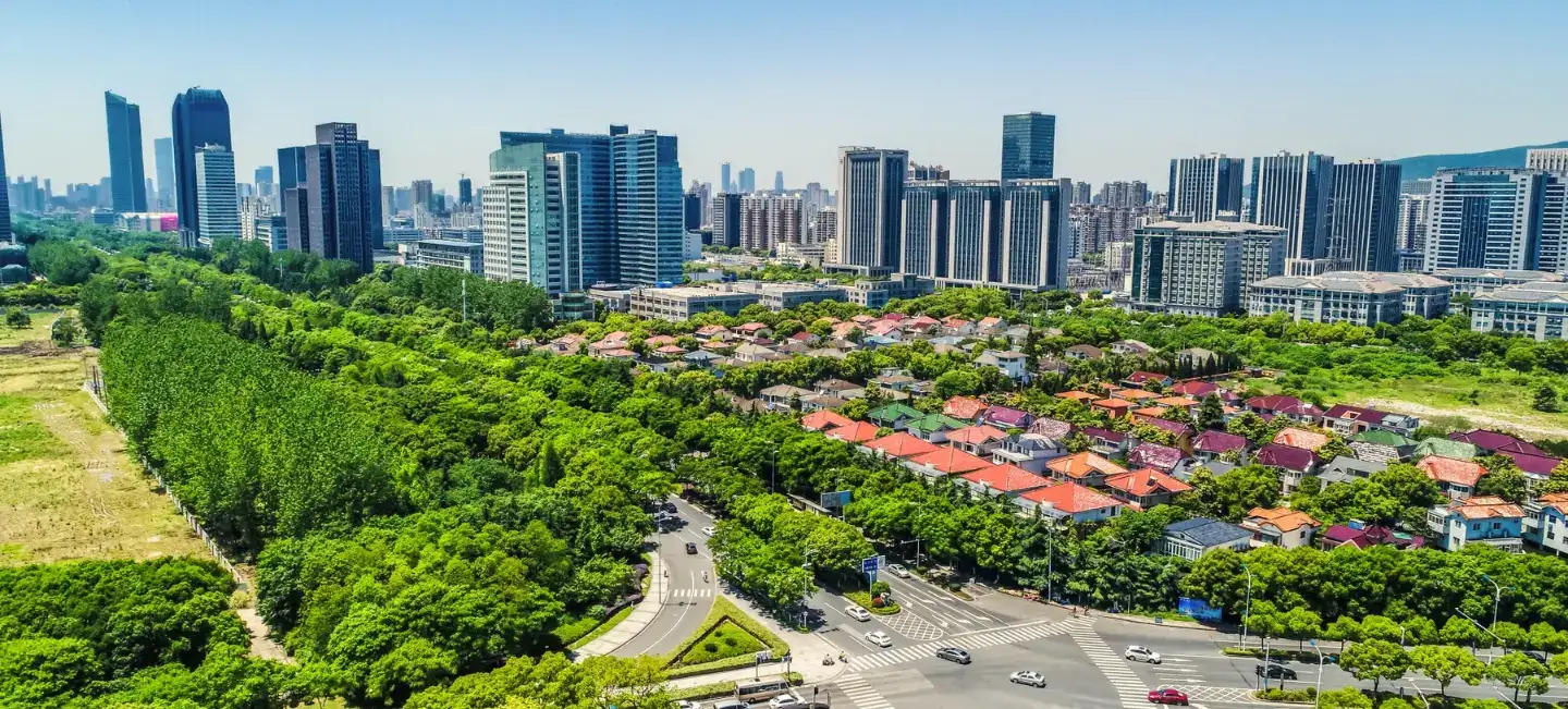 Pemandangan bandar dengan bangunan tinggi, taman dan rumah di bawah langit cerah.