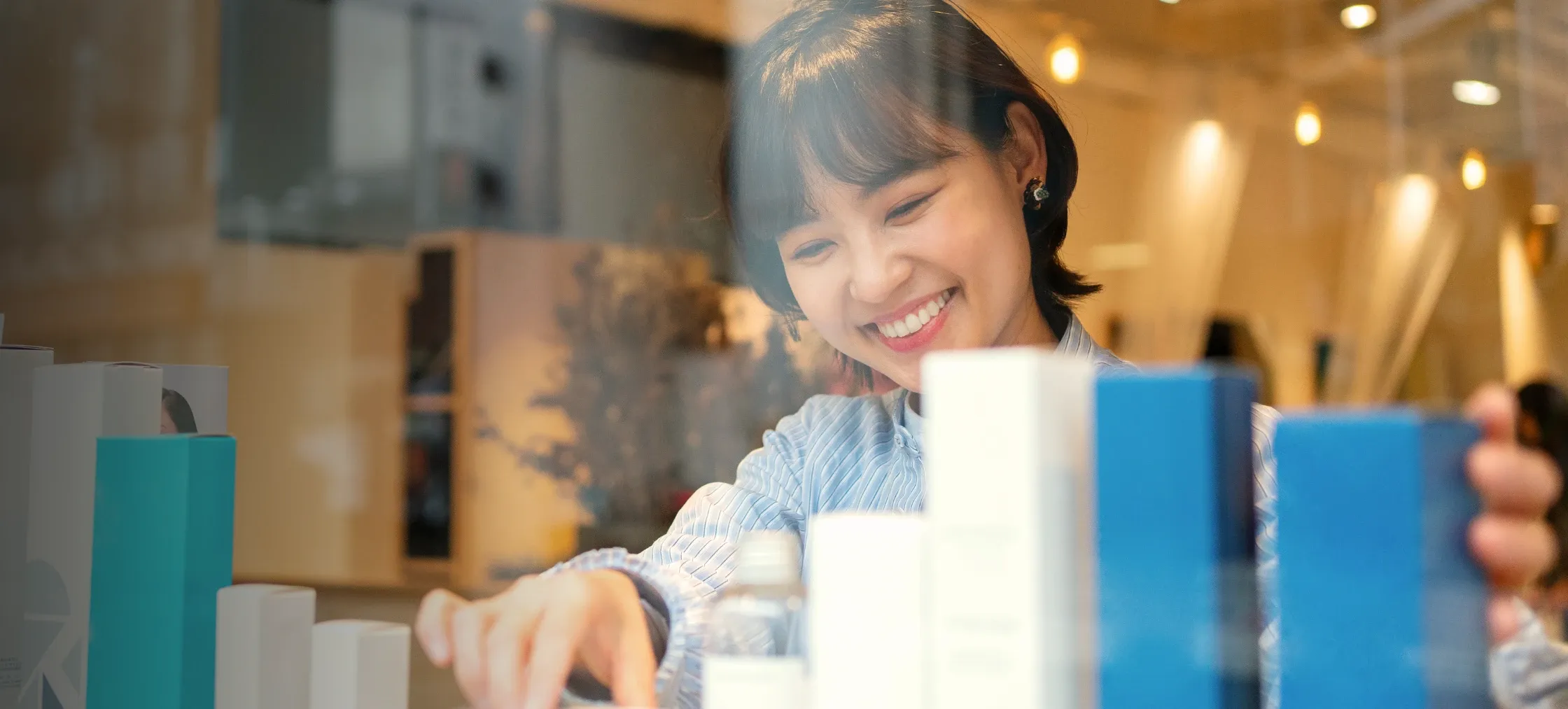 Wanita muda tersenyum melayari produk di rak dalam kedai runcit yang cerah